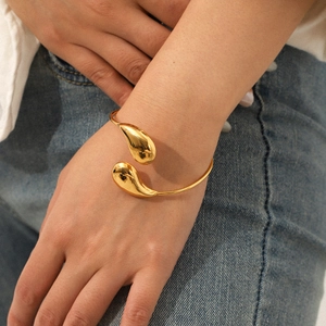 Detail of 18k gold plated teardrop open bangle worn by a model in casual white shirt