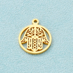 Macro shot of a gold-plated circular hollow Hamsa hand pendant charm on a textured blue surface