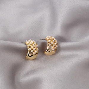 Detailed shot of gold-plated pearl stud earrings on textured grey silk background