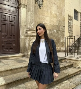 Street style view of a dark blue denim jacket paired with a pleated skirt and crossbody bag