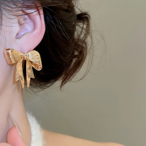Primo piano dell'orecchino a fiocco dorato con texture a nastro su modella