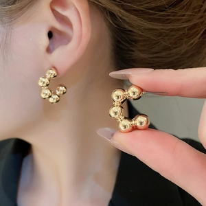 Macro shot of gold C-shaped beaded stud earrings showcasing polished metal texture