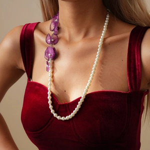Close-up of pearl necklace with purple chiffon flower on model wearing burgundy dress