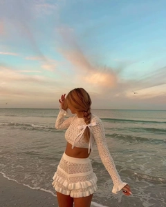 Detail of white knit two-piece set featuring long-sleeved crop top with bow and ruffled skirt
