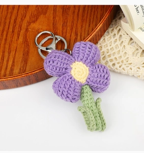 Detailed close-up of handmade purple knitted flower keychain on a wooden tray