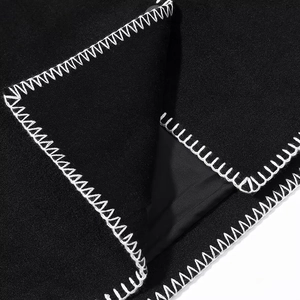 Détail macro des coutures blanches en zigzag sur le tissu en laine noire de la veste