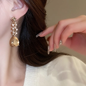Close-up of elegant gold earrings with teardrop champagne stones worn by a model