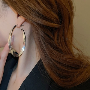 Close-up of model wearing large oval silver hoop earrings in a minimalist fashion style
