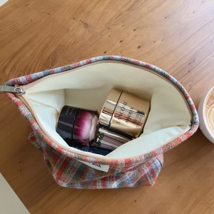 Plaid tweed makeup bag with silver zipper and spacious interior on a wooden desk