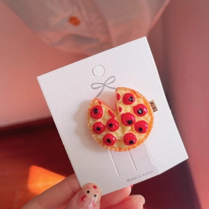 Detailed view of a handmade simulation pizza hair clip on a white decorative card