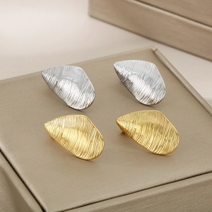 Detail showing textured gold and silver irregular leaf earrings on a jewelry box display