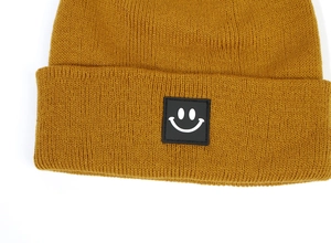 Dettaglio del berretto in maglia a coste giallo zenzero con una toppa a sorriso nera