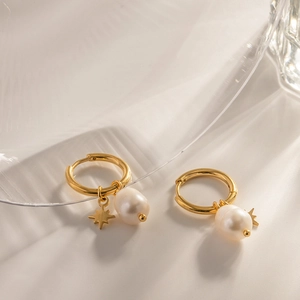 Détail de boucles d'oreilles étoile dorée avec perles d'eau douce sur surface en pierre