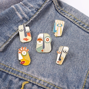 Set of five colorful Picasso style abstract face enamel pins on blue denim fabric texture