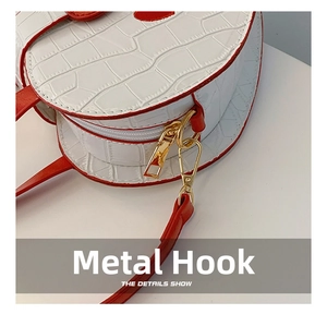 Detail show of golden metal hook on white crocodile leather bag with red trim