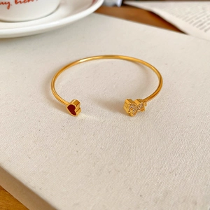 Close-up of golden bangle with a red enamel heart and zircon-studded bow detail
