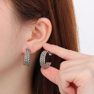 Detailed view of silver C-shaped twisted earrings on model showing woven texture