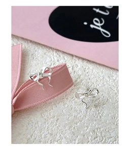 Macro shot of silver bow stud earrings on white texture with pink ribbon and je t'aime card