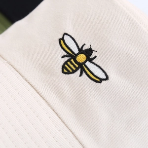 Beige cotton bucket hat featuring detailed bee embroidery and twill fabric texture