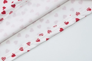 Gros plan des coutures surjetées et des motifs de cœurs rouges sur tissu blanc