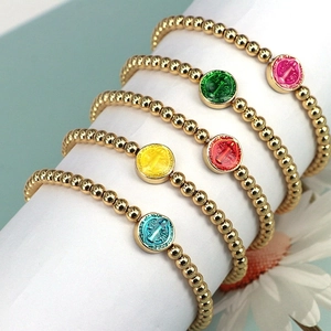 Close-up of colorful enamel religious medals on beaded gold bracelets set on a pedestal