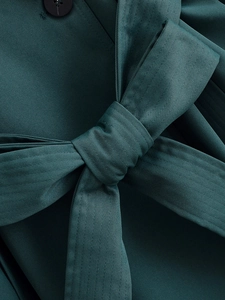 Detailed macro view of dark green twill fabric texture with belted waist and button closure