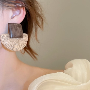 Detail of wooden rectangle and beige raffia semicircular drop earrings on model