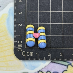 Macro shot of 2cm blue-yellow striped resin H-shaped accessory with pink heart detail