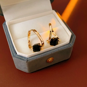 Macro shot of minimalist gold earrings with black square stones in a blue velvet box