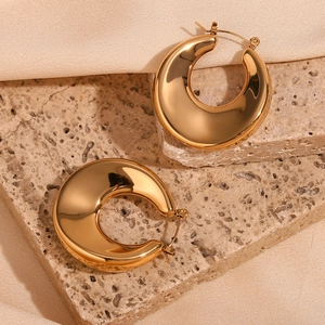Close-up of chunky gold hoop earrings with mirror polish finish on stone background
