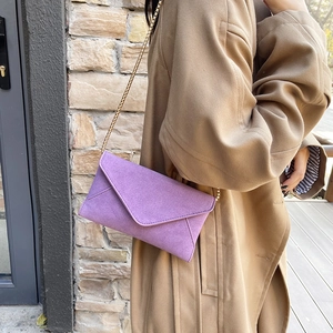 Purple velvet envelope crossbody bag with gold chain strap worn by a model in a trench coat