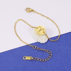 Bracelet minimaliste en acier doré avec pendentif ajouré Bélier posé sur un coquillage