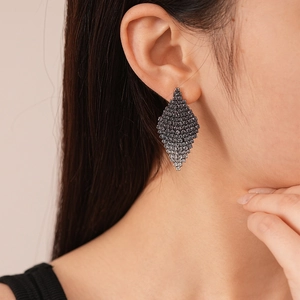 Close-up of geometric diamond-shaped earrings with dark grey crystals on a model