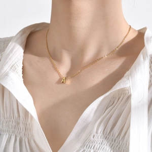 Vista detallada de un collar con colgante de letra A dorada llevado por una modelo en blanco