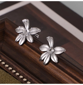Macro shot of silver orchid flower earrings on a vintage wood tray with polished finish