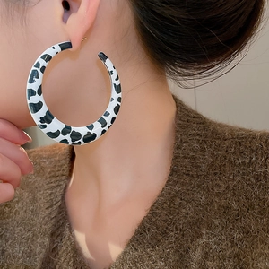 Close-up of model wearing large C-shaped earrings with black and white cow print pattern