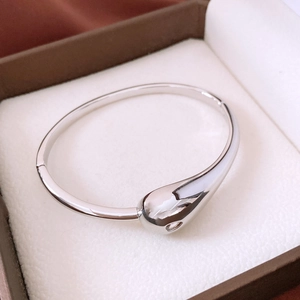 Macro shot of silver teardrop bangle resting on a luxury textured jewelry box cushion