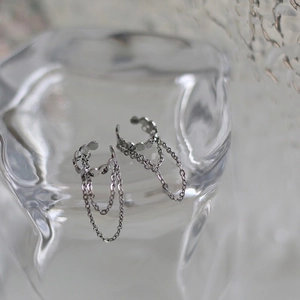 Detail of silver ear bone cuff with three dangling thin chains on textured glass