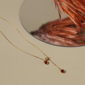 Detailed shot of a gold heart tassel necklace with red pendants on a textured surface