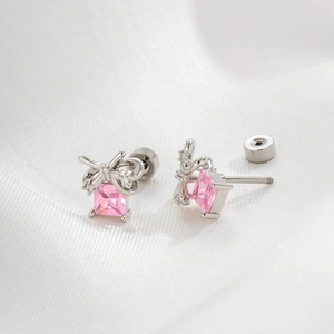 Elegant silver bow earrings with pink square zircon stones on soft white silk backdrop
