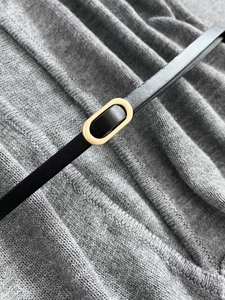 Detail of a slim black leather belt featuring a polished gold oval metal buckle