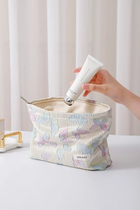 Detailansicht der Schmetterlingsstickerei auf einer cremefarbenen Kosmetiktasche