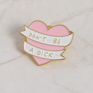 Pink heart enamel pin with gold metal trim featuring the slogan DON'T BE A DICK.