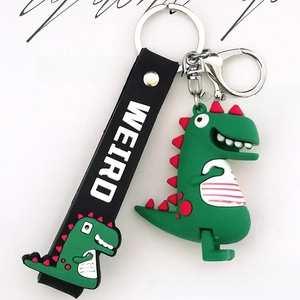 Close-up of green cartoon dinosaur keychain with black Weird wrist strap and silver clasp
