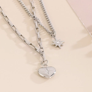 Detail of silver double-layered necklace with heart and starburst charms on a paperclip chain