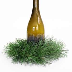 Artificial green pine needle wreath for Christmas table decoration around a glass bottle