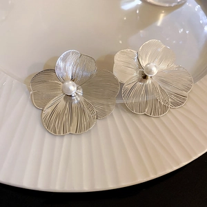 Macro detail of silver flower earrings with textured petals and a centered pearl inlay