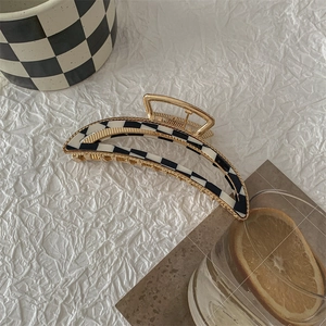 Macro detail of a large checkered hair claw clip with golden frame on a white background