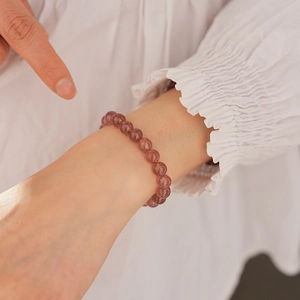 Detail of pink strawberry quartz bead bracelet worn on wrist against white fabric