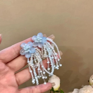 Detail of blue crystal flower earrings with dangling bead tassels held in hand